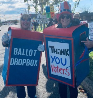 Two women in homemade ballot drop box costumes, one holding a Thank You Voters sign